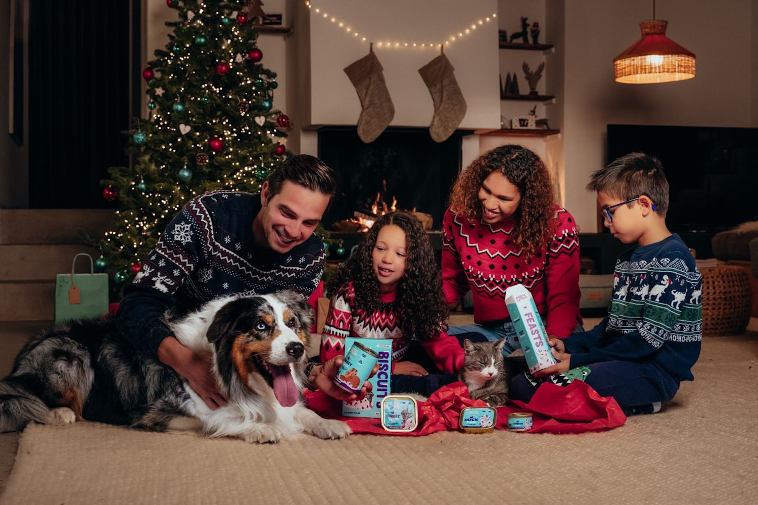 Family in festive christmas clothing with the pet dog around the christmas tree.