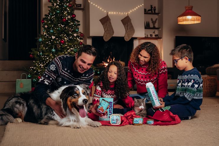 Family in festive christmas clothing with the pet dog around the christmas tree.